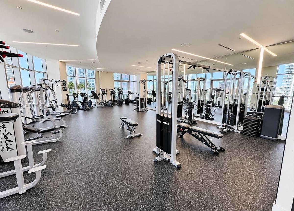 Fitness center featuring floor-to-ceiling windows, rubberized flooring, recessed linear lighting, and wall-to-wall mirrors