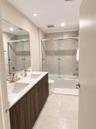 Dual-sink vanity with wood-finish cabinetry, quartz countertop, large wall-mounted mirror, and tub-shower combination featuring sliding glass doors an