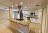 Kitchen featuring an island with a built-in cooktop and stainless steel vent hood, granite countertops, white cabinetry with silver hardware, stainles