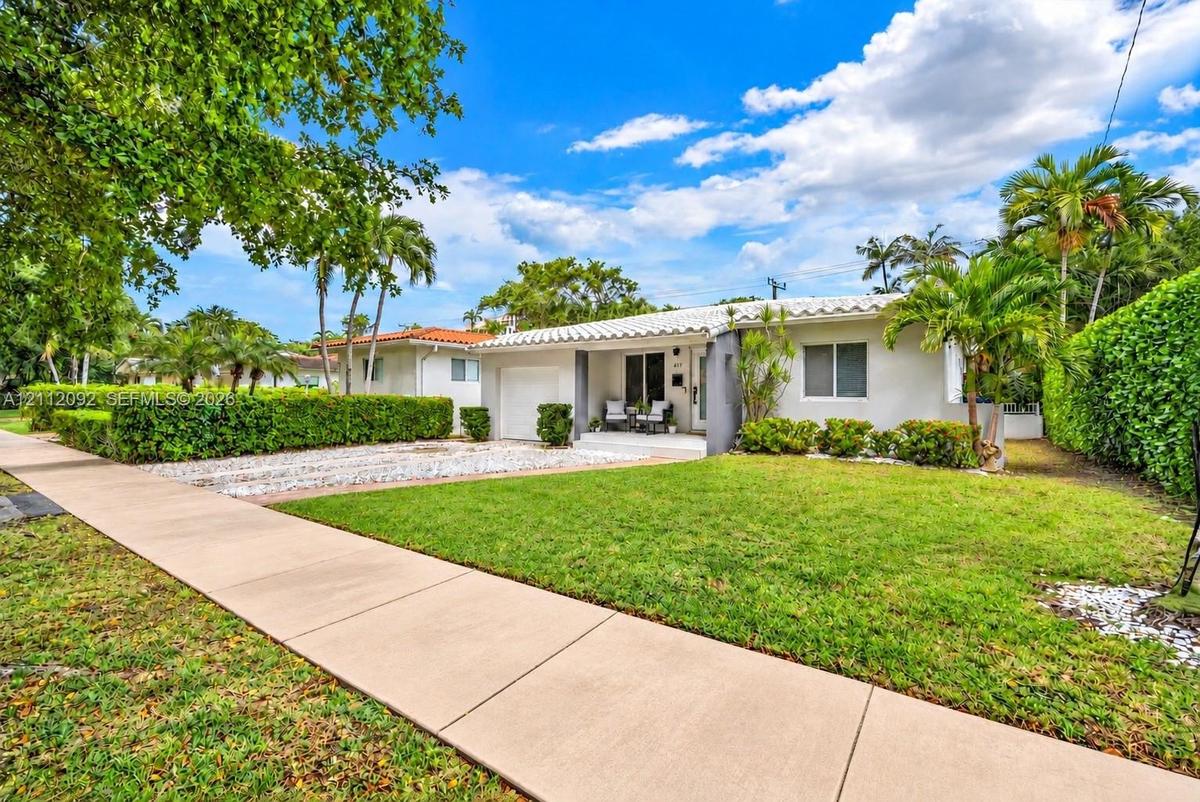 Single-story residence featuring a tile roof, light-toned exterior finish, attached garage, manicured lawn, and established landscaping
