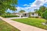 Single-story residence featuring a tile roof, light-toned exterior finish, attached garage, manicured lawn, and established landscaping