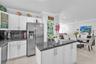 Kitchen featuring white shaker-style cabinetry, dark stone countertops, stainless steel appliances, a brass-toned gooseneck faucet, and a frosted glas