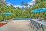 In-ground swimming pool with a tiled perimeter, expansive stone-finish patio, and mature palm landscaping