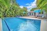 Private outdoor space featuring a rectangular swimming pool, expansive natural stone patio, and perimeter lush tropical landscaping