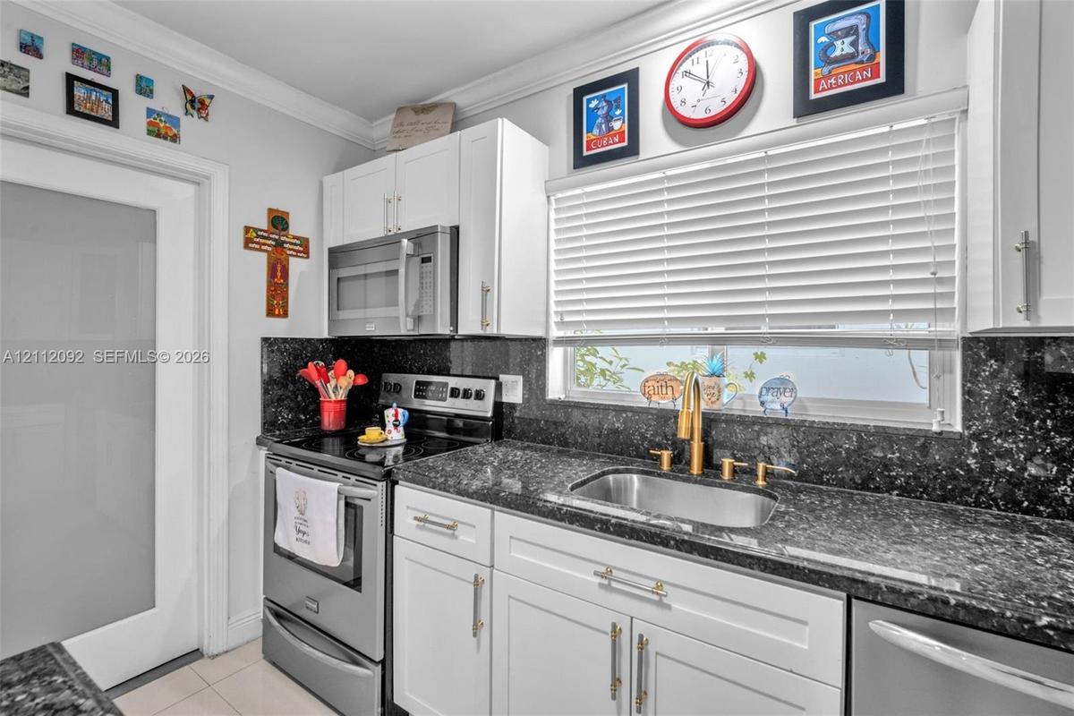 Open-concept interior featuring large-format tile flooring, recessed lighting, and a kitchen with white cabinetry, a center island with dark counterto