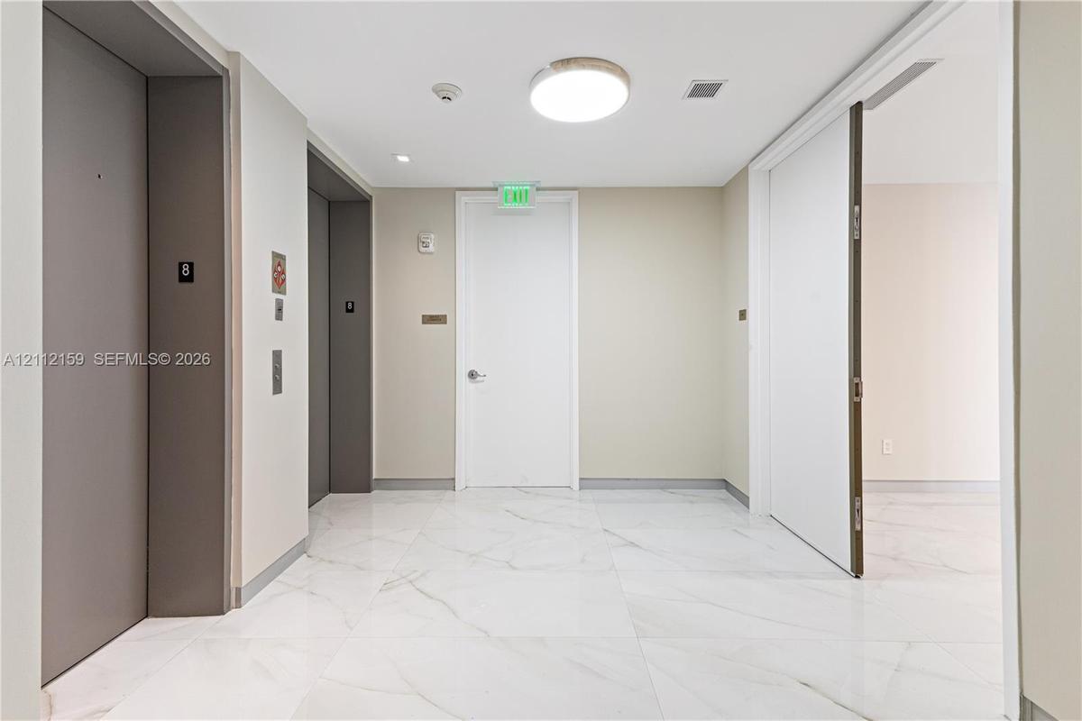 Common area featuring large-format white stone-finish tile flooring, dual elevators with metallic finishes, and recessed ceiling lighting