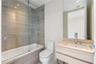 Bathroom featuring a wall-mounted vanity with integrated sink, glass-enclosed tub with handheld shower fixture, and horizontal tile wall surrounds