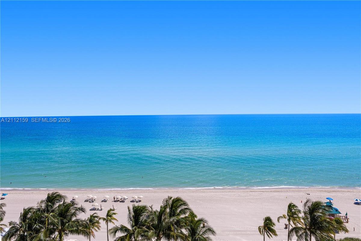Oceanfront perspective featuring a wide sandy beach, turquoise waters, and mature palm trees