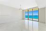 Polished stone flooring, crystal-accented chandelier, floor-to-ceiling glass sliding doors, and private balcony with ocean backdrop