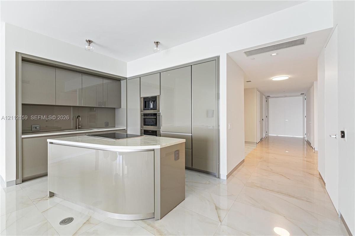 Kitchen featuring high-gloss cabinetry, stone-surface center island with integrated cooktop, built-in double wall oven, and large-format tile flooring