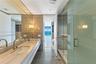 Dual vanity with wood-finish cabinetry, rectangular vessel sinks, floor-to-ceiling mirror, glass-enclosed shower, and polished stone flooring