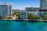 Waterfront mid-rise building featuring floor-to-ceiling glass windows, exterior balconies with glass railings, and concrete bulkhead