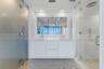 Double vanity with white cabinetry, integrated sinks, wall-mounted faucets, expansive mirrored medicine cabinet, and glass-enclosed shower with rainfa