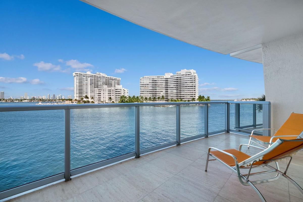 Covered balcony featuring stone flooring and a glass-paneled railing overlooking the water