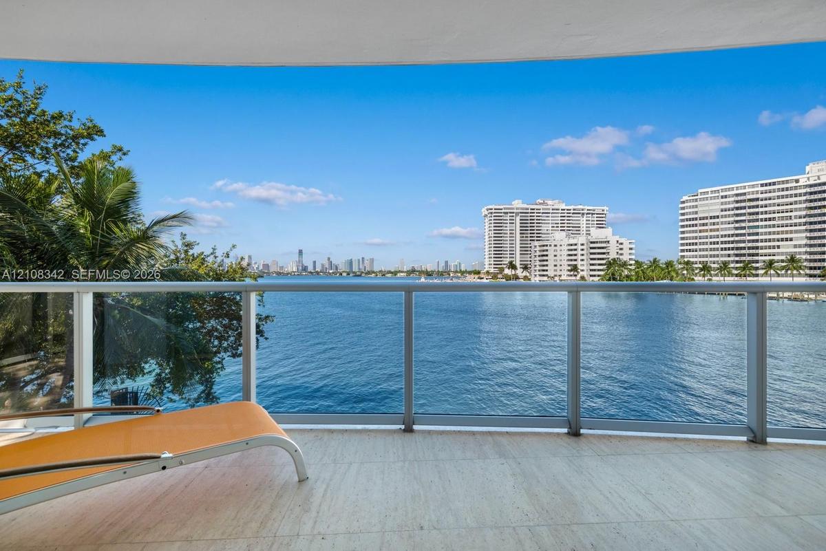 Covered balcony featuring stone flooring and a glass-paneled railing overlooking the water