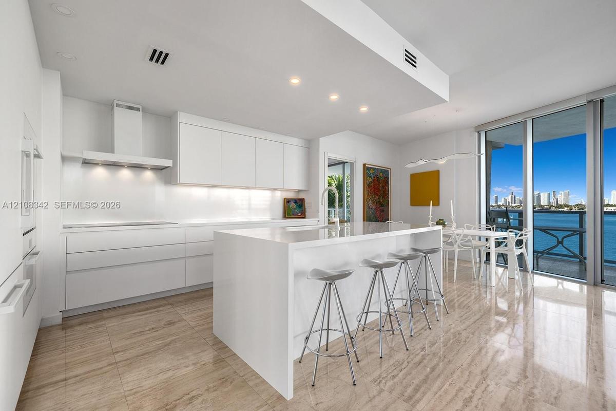 Contemporary kitchen featuring sleek flat-panel cabinetry, a waterfall-edge stone island, built-in stainless steel appliances, stone flooring, and flo