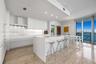 Contemporary kitchen featuring sleek flat-panel cabinetry, a waterfall-edge stone island, built-in stainless steel appliances, stone flooring, and flo