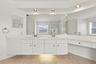 An impressive primary bathroom featuring an extended vanity with abundant cabinetry, expansive mirrors, recessed lighting, and a dedicated makeup stat