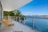 Covered balcony featuring stone flooring and a glass railing with metal framing, overlooking the waterfront and city skyline