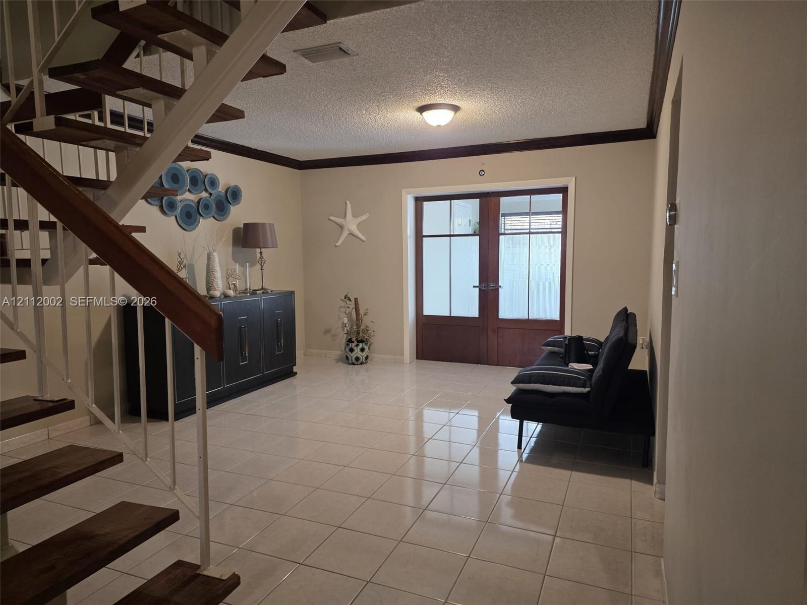 Open foyer featuring wood-tread staircase, white metal railings, ceramic tile flooring, and double-entry doors with glass paneling