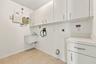 Conveniently located on the first floor, this dedicated laundry room features abundant overhead cabinetry, a utility sink, neutral tile flooring, and 