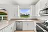 White cabinetry, stainless steel appliances, and generous counter space complement a large kitchen window overlooking the beautifully landscaped outdo