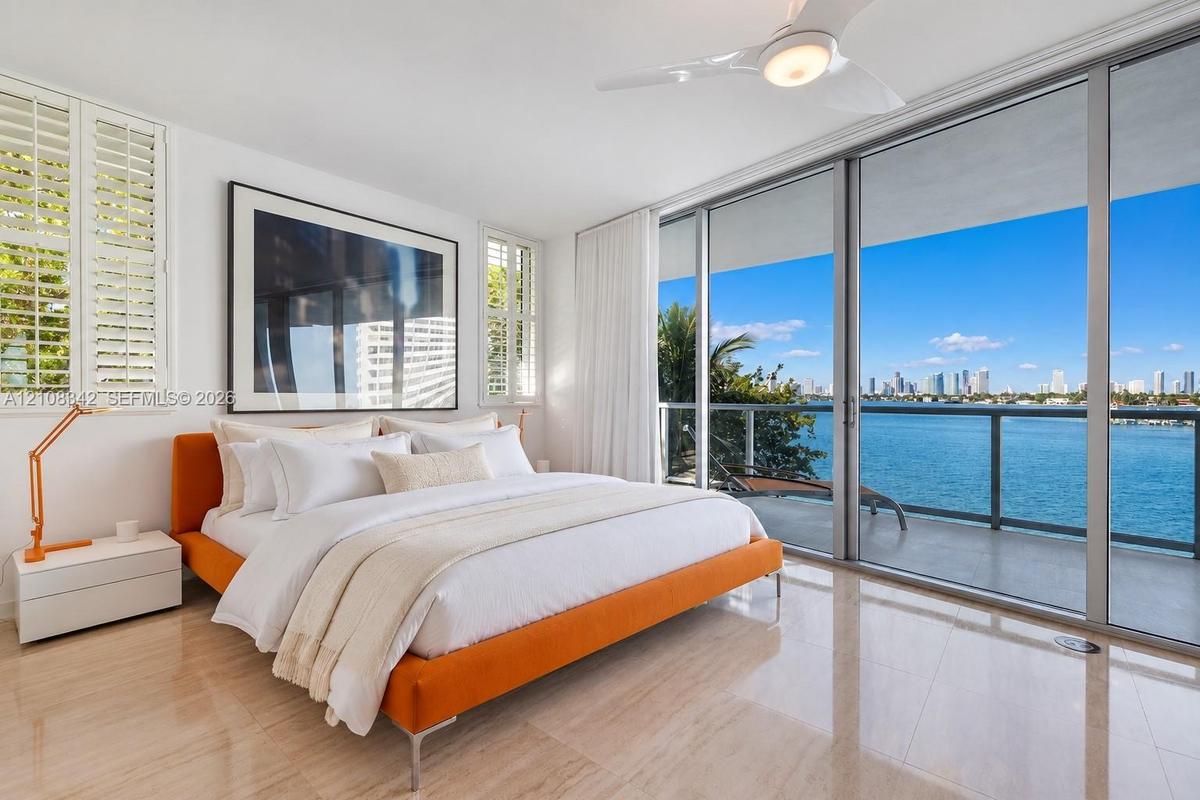 Floor-to-ceiling sliding glass doors, private balcony with metal railing, polished stone flooring, custom plantation shutters, and ceiling fan with in