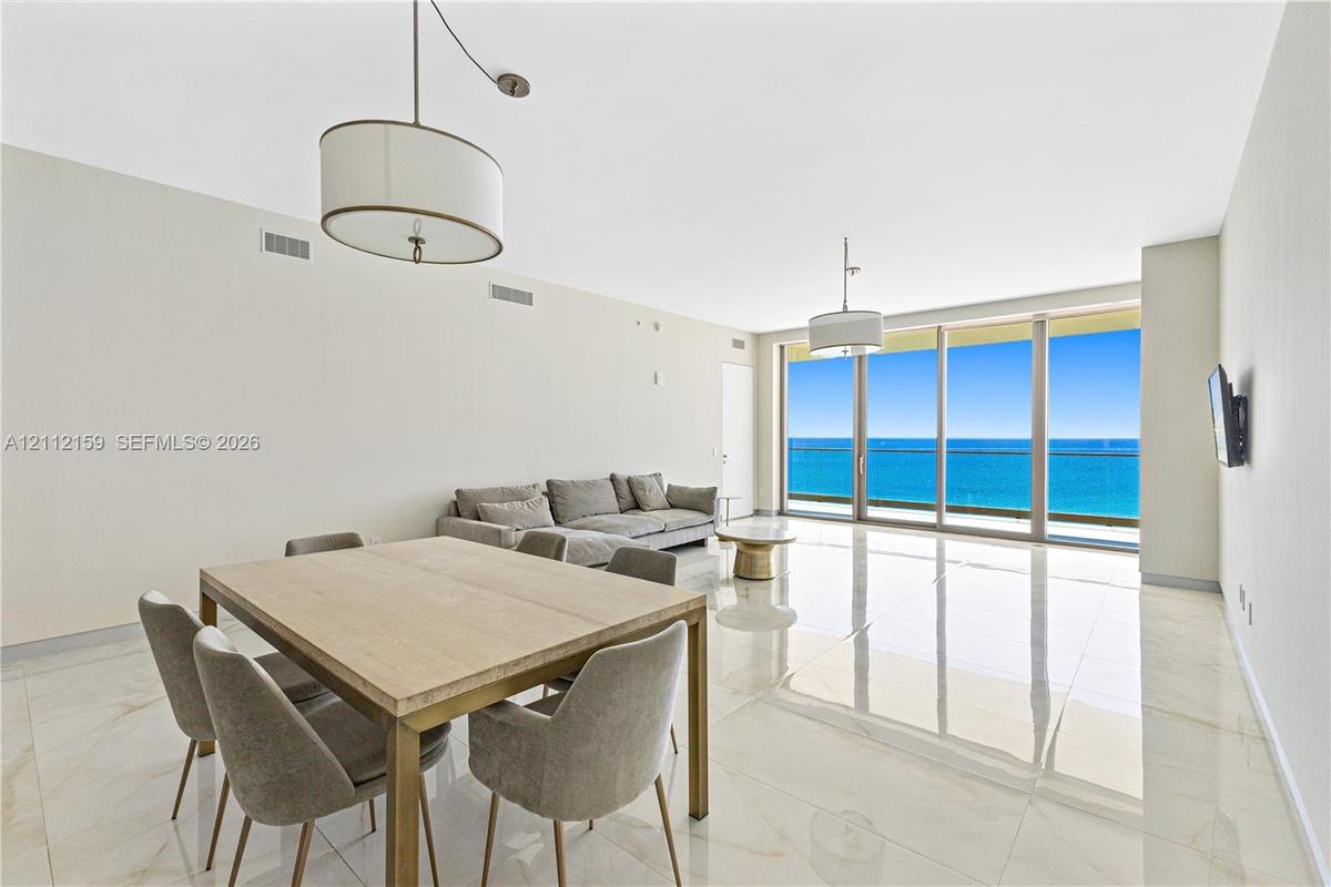 Floor-to-ceiling glass panel windows, polished tile flooring, pendant lighting fixtures, and an exterior balcony