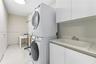 Laundry space featuring stacked front-load laundry appliances, white cabinetry with integrated sink, and polished tile flooring