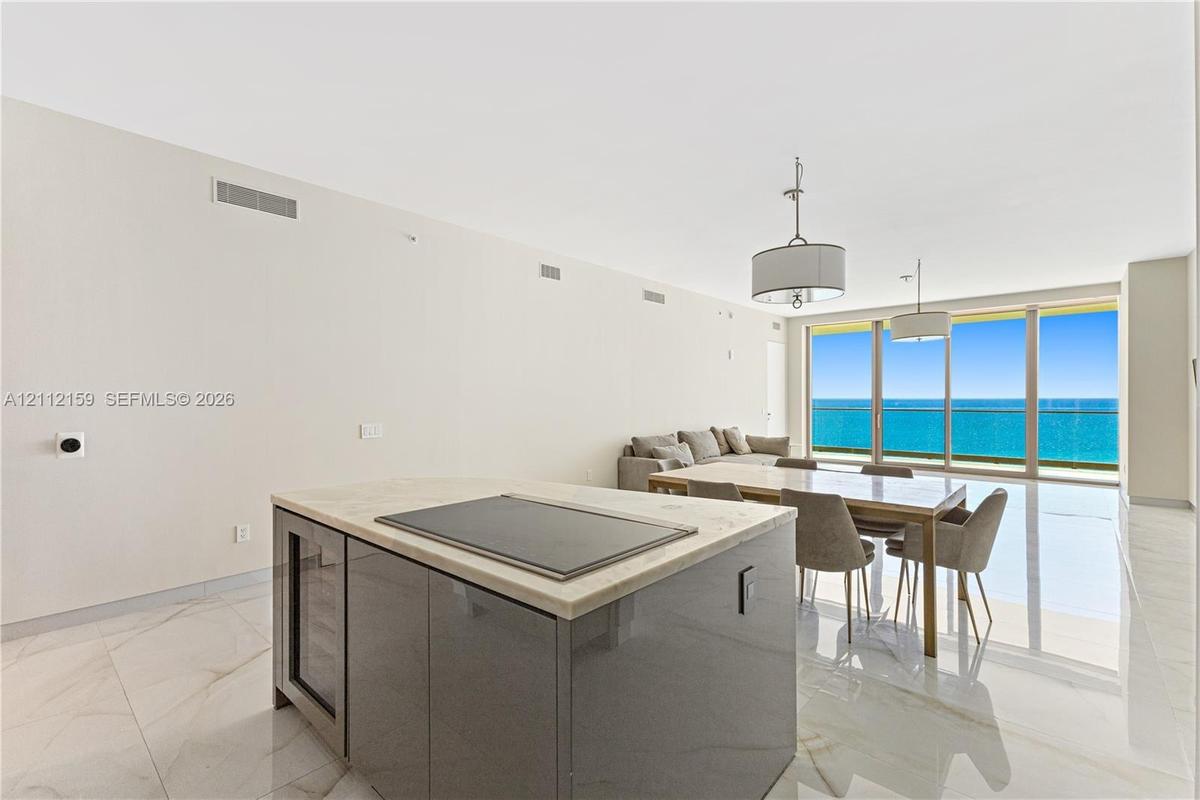 Open-concept interior featuring large-format stone-look flooring, center island with stone countertop and built-in wine refrigeration, dual drum penda