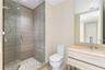 Walk-in shower with wood-finish tile surround and glass enclosure, floating vanity with integrated rectangular sink, wall-mounted faucet, and flush-mo