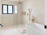 Freestanding soaking tub with brass fixtures, glass-enclosed walk-in shower, dual recessed wall niches, and matte-finish plaster wall treatment