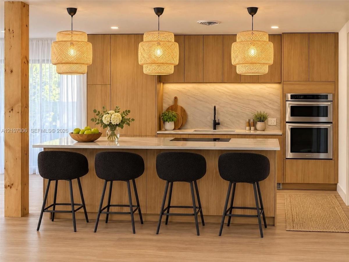 Kitchen featuring flat-panel wood cabinetry, integrated double wall ovens, a large island with stone-finish countertop, textured pendant lighting, and