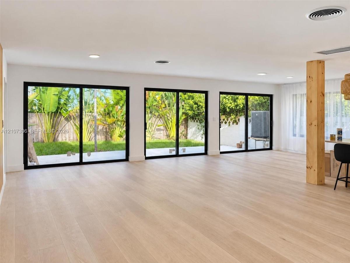 Interior space featuring three sets of black-framed sliding glass doors, light-toned wood-finish flooring, recessed ceiling lighting, and an exposed s