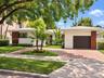 Single-story residence featuring a crisp white exterior with vertical wood-accented columns, a paved brick driveway, a dedicated garage, and mature la