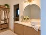 Custom wood-finish vanity with a neutral stone countertop, white vessel sink, arched wall mirror, and integrated gold-toned vanity lighting