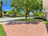Brick-paver driveway with a herringbone pattern, mature trees, manicured lawn, and perimeter landscaping