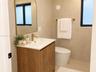 Wood-finish vanity cabinet with a white basin, arched wall mirror, brass-toned faucet, and hardware, complemented by textured wall finishes and a dual