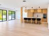 Kitchen featuring flat-panel wood cabinetry, a central island with a solid-surface countertop, built-in double ovens, wood-finish flooring, and dual s