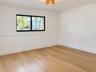 Room featuring wood-finish flooring, white walls, black-framed horizontal window, and a woven drum light fixture