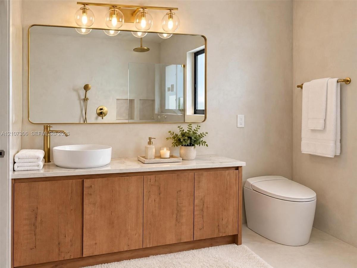 Bathroom vanity featuring a wood-finish cabinet, stone-top surface, vessel sink, and brass fixtures, complemented by a large gold-framed wall mirror w