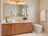 Bathroom vanity featuring a wood-finish cabinet, stone-top surface, vessel sink, and brass fixtures, complemented by a large gold-framed wall mirror w