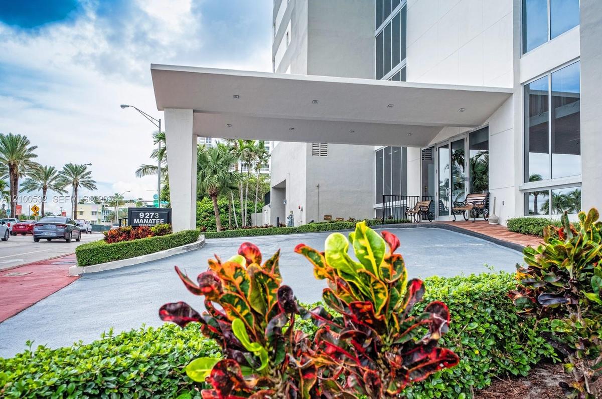 Covered porte-cochère entry featuring recessed lighting, glass-paneled entrance doors, multi-story building facade, and manicured landscaping