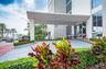 Covered porte-cochère entry featuring recessed lighting, glass-paneled entrance doors, multi-story building facade, and manicured landscaping