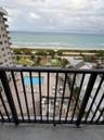 Balcony featuring a black metal railing, overlooking a swimming pool, landscaped grounds, and the ocean shoreline