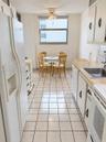Galley kitchen featuring white cabinetry, light-toned countertops, ceramic tile flooring, a built-in stainless steel sink, and a ceiling-mounted light