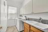 Laundry space featuring stone-composite countertop, dual-basin drop-in sink, chrome pull-down faucet, wooden base cabinetry, and overhead storage cabi