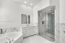 White vanity with integrated basin, framed wall mirror, soaking tub with deck-mounted faucet, walk-in shower with glass enclosure, and patterned tile 