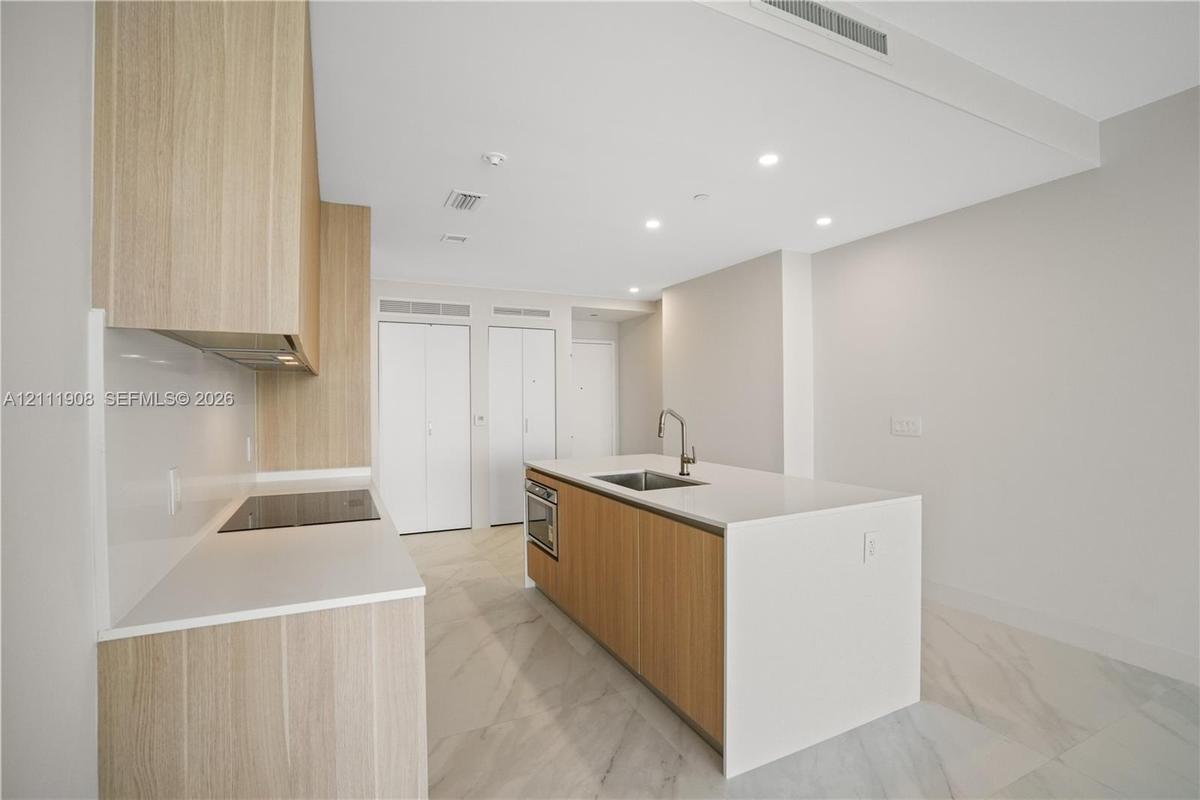 Kitchen featuring wood-finish cabinetry, an island with a stone-surface countertop, an integrated electric cooktop, and large-format tile flooring