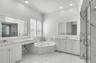 Bathroom featuring white cabinetry, integrated vanity, dual-basin sinks, jetted soaking tub, and stone-accented shower enclosure with glass door